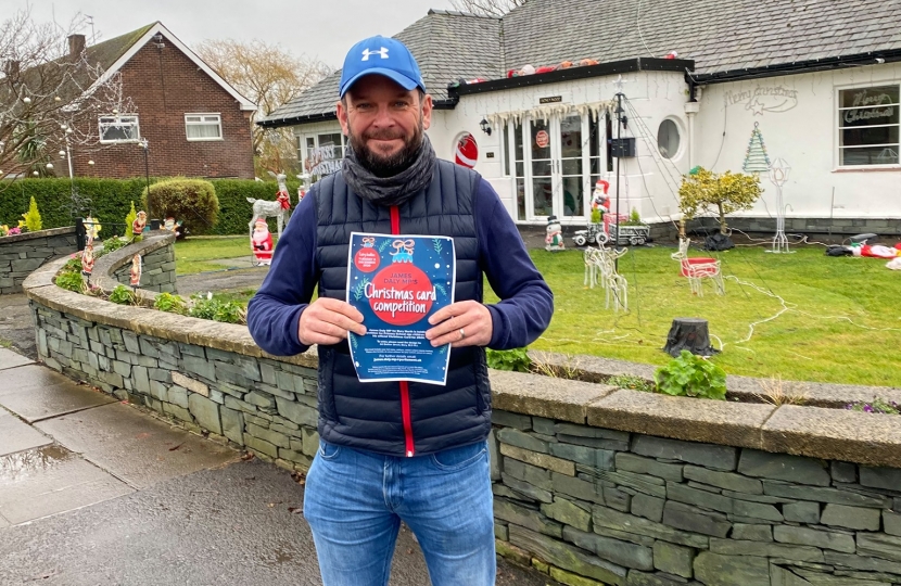 James Daly stands in front of a house decorated for Christmas with his Christmas Card Competition poster