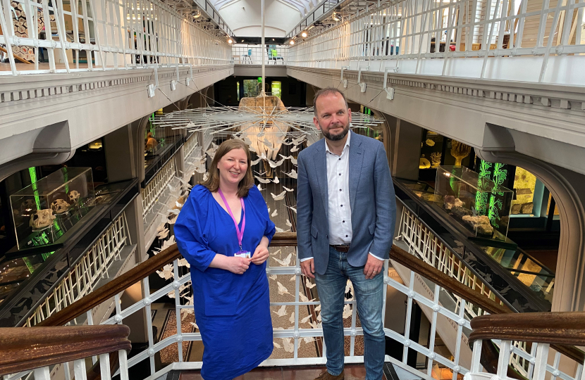 James Daly MP and George Young, Head of Exhibitions and Collections, stand on a staircase with the Manchester Museum Interior behind them